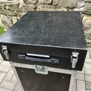Černý transportní kufr s kovovými hranami a zapojovacími zámky. Na přední straně je nápis Soundcraft Spirit Folio SX a černá rukojeť. Povrch víka vyk…