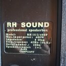 Fotografie detailu zadní strany reproduktorové skříně s černým povrchem. Na ní je nalepený štítek s nápisy: RH SOUND, professional speakerbox, Model:…