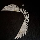 Detail černého povrchu s texturou kůže. Je na něm bílý potisk ve tvaru křídel s nápisem DEAN. Barva potisku je v některých místech opotřebovaná a žlu…