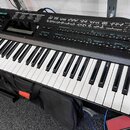 Černý digitální syntezátor s bílými a černými klávesami. V levém horním rohu je bílý nápis YAMAHA a pod ním model DX7 IIFD. Horní panel obsahuje řadu…