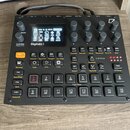 Černý digitální sampler Digitakt II s displejem a ovládacími prvky. Na přední straně je nápis Digitakt II a řada tlačítek, otočných knoflíků a vstupn…