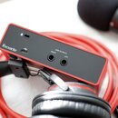 Červený audio interface s černým zadním panelem. Na panelu je bílý nápis Focusrite, USB port a dva výstupy s popisky LINE OUTPUTS RIGHT a LEFT. Vedle…