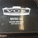 Černá papírová krabice s bílým potiskem. Uprostřed je logo VOX v rámci grafického elementu a pod ním nápis AMPLIFICATION LTD. Dole jsou uvedeny označ…