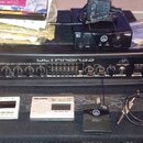 Na fotografii je černý basový zesilovač s nápisem ULTIMABASS a označením BX3000H 300-WATT 2-CHANNEL BASS AMPLIFIER HEAD značky behringer. Nad ním lež…