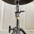 Detail spodní strany sedáku a chromovaného stojanu. Na středovém sloupku je žlutý štítek s nápisem "DRUM STAND" a logem "ittah". Povrch chromu vykazu…