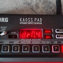 Černý efektový procesor KORG KAOSS PAD DYNAMIC EFFECT/SAMPLER. Zařízení má červený digitální displej, několik ovládacích knoflíků a řadu tlačítek s č…