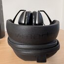 Černé sluchátka s polstrovaným náhlavním pásem a mušlemi. Na náhlavním pásu je vyražen nápis v-moda. Sluchátka jsou umístěna na černém zipovém pouzdř…