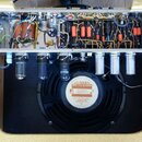 Fotografie zachycuje vnitřek kytarového komba. V horní části je vidět elektronika s kondenzátory a zapojením, ve spodní části je umístěn reproduktor…