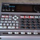 Stříbrný elektronický doprovodný automat značky BOSS, model Dr. Rhythm DR-890. Zařízení má digitální displej, ovládací knoflík VALUE a množství tlačí…