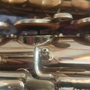 Detailní záběr na mechanismus saxofonu s lakovaným zlatavým povrchem. Jsou vidět klapky s hnědými polštářky a kovové spojovací mechanismy. Na povrchu…