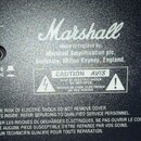 Detail zadní strany černého přístroje s texturou. Uprostřed je bílé logo Marshall a nápis Made in England by: Marshall Amplification plc, Bletchley,…