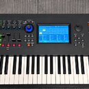 Černý digitální klavír s bílými a černými klávesami. Na levé straně je logo YAMAHA, vpravo nápis MODX6/7/8 a tabulka s popisem funkcí. Nástroj má ovl…