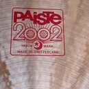 Detailní záběr na povrch činely s koncentrickými rýhami. Uprostřed je červený hranatý štítek s bílým textem PAiste 2002, TRADE MARK a MADE IN SWITZER…