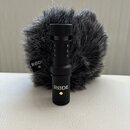 Černý mikrofon s nápisem RØDE umístěný před šedým chlupatým windscreenem. Na windscreenu je rovněž viditelné logo RØDE. Povrch mikrofonu je matný a v…