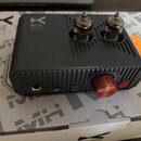 Šedý stolní zesilovač s dvěma viditelnými vakuovými elektrony na horní straně. Na přední straně je červený ovratový knoflík, červené tlačítko a tři k…