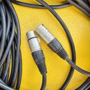 Dva černé audio kabely s kovovými konektory typu XLR. Na povrchu jednoho z kabelů je čitelný nápis PHL MICROPHONE CABLE. Kovové části konektorů vykaz…