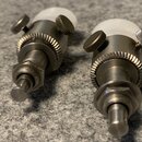 Dvě kovové ladicí mechaniky s bílými plastovými knoflíky. Jsou vyrobeny z tmavého kovu s rýhovaným prstencem a dvěma malými zoubkovanými šrouby. Na s…