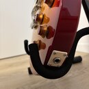 Detail elektrické kytary v červeném gradientním lakování, umístěné na černém stojanu. Na těle jsou vidět čtyři hnědé vřetenové knofíky a kovová zásuv…