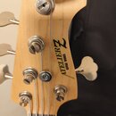 Detail hlavy světle hnědé dřevěné basové kytary s pěti ladicími kolíky. Na dřevě je černý nápis ATELIER Z a pod ním menší text GUITAR WORKS. Povrch d…