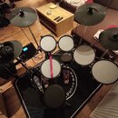 Elektronická bicí souprava s černými pady a činely, umístěná na černém koberci. Na koberci je viditelný bílý nápis „www.sound“. Souprava obsahuje něk…