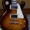 Elektrická kytara s tónem sunburst, bílým pickguardem a dvěma humbuckery. Na přepínači je vidět nápis RHYTHM a TREBLE. Kytara má čtyři zlaté ovládací…