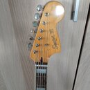 Fotografie zachycuje hlavu a hриф kytary z přírodního dřeva s lakovaným povrchem. Na hlavě je černý nápis Squier VI by Fender. Nástroj má šest ladicí…