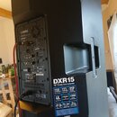 Černý aktivní reproduktor značky YAMAHA, model DXR15. Na zadní straně je vidět ovládací panel s konektory a nápisy, včetně označení "DXR15" a loga "Y…