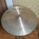 Kruhové činely typu ride z mosazného kovu s viditelnými stopami používání a drobnými škrábancemi. Na povrchu je nápis istanbul Agop Handmade cymbals…