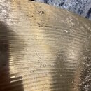 Detail zlatavého kovového činely s viditelným broušením povrchu. V centru je vyražen nápis SABIAN v oblouku a pod ním slovo CANADA. Povrch vykazuje z…