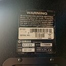 Detailní záběr na zadní stranu černého reproduktoru s dvěma nálepkami. Horní nálepka obsahuje varovný text „WARNING“ a označení „S112V“, čárcový kód…