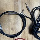 Dvě černé audio kabeláže s kovovými konektory typu jack. Na jednom z kabelů je viditelný malý obdélníkový štítek s nápisem MXR. Druhý kabel má na pov…