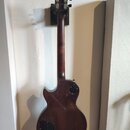 Zadní strana elektrické kytary s tmavě hnědým povrchem a tvarem Les Paul. Na zadní straně těla je vidět černý plastový kryt elektroniky a kruhový otv…