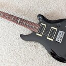 Černá elektrická kytara s dvojstupňovými humbuckery a fixačním mostem. Na hrazdici jsou viditelné vložky ve tvaru ptáků a na hlavě je nápis PRS. Povr…