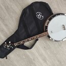Bílá banjo s hnědým hřednou a kovovým rímcem, položené na černé softcase kabelce s bílým logem XS. Na hmatníku jsou viditelné vložky ve tvaru hvězd a…