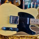 Kytara typu Telecaster v krémové barvě s černým pickguardem a hnědým javorovým hmatníkem. Na kovovém krytu snímače je nečitelný nápis. Nástroj leží v…