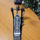 Černý basový pedál s kovovou stlačovací deskou. Na desce je vyražen nápis dw 7000 a pod ním text The Drummer's Choice. Pedál je vybaven řetízkovým po…