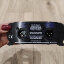 Černý elektronický přístroj s dvěma XLR konektory. Na povrchu jsou bílé texty: „MAIN MIC OUTPUT“, „ISOLATED OUTPUT (SETTER)“, „CE“ a instrukce k funk…