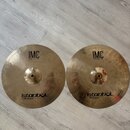 Dvě mosazné činely typu hi-hat položené vedle sebe na světlé podlaze. Oba mají identické nápisy: v horní části „IMC 13" BRILLIANT HI-HAT“ a v dolní č…
