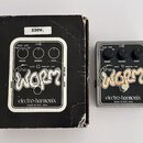 Fotografie zobrazuje kytarový efekt a jeho původní černou krabici. Na obou je vidět nápis „the WORM“ a značka „electro-harmonix MADE IN NYC, USA“. Ef…
