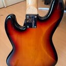 Zadní strana elektrické kytary s tělem v provedení sunburst (oranžová a černá). Kytara má světlý dřevěný hridel a černý kryt elektroniky s čtyřmi šro…