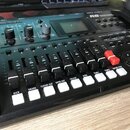 Černý elektronický bicí modul s LCD displejem a řadou posuvníků. Na horním panelu jsou viditelné nápisy ZOOM, R8 a označení vstupů INPUT 1, INPUT 2.…