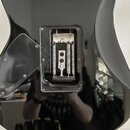 Zadní strana černé kytary s lesklým povrchem. V těle je vyveden obdélníkový otvor, ve kterém jsou vidět pružiny a mechanismus tremola. Vedle otvoru j…