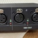 Černý elektronický přístroj s čtyřmi konektory DMX OUT. Nad konektory jsou čísla 3 a 4, u každého vstupu jsou umístěny zelená a červená kontrolka. Vp…