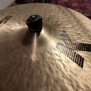 Záběr na povrch mosazného činely s výrazným kladeným povrchem. Na nástroji je černý nápis DARK CRASH a pod ním menší text 16"/40 cm hand hammered. V…