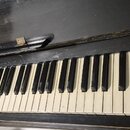 Klávesnice černého pianina s bílými a černými klávesami. Povrch černého laku nad klávesnicí vykazuje známky opotřebení a škrábance. Na horním dřevěné…