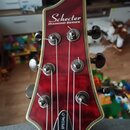 Hlava elektrické kytary v tmavě červené barvě s bílým lemováním. V horní části je bílý nápis Schecter a pod ním DIAMOND SERIES, v dolní části je svis…