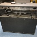 Zadní strana černého kytarového komba s kovovou mřížkou a přívodním kabelem. Na zadním panelu je logo Fender, nápis SERIAL NUMBER T0 524813 a text A…