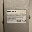 Spodní strana stříbrného kovového efektpedálu. Na bílém štítku je logo NUX, web www.nuxaudio.com a nápis AC ADAPTER: DC 9V s grafickým znázorněním po…