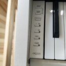 Detail bílého digitálního piana s viditelnými klávesami. Na ovládacím panelu jsou tlačítka s nápisy DEMO/SONG, PIANO/VOICE, METRONOME, + R, - L, REC.…