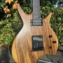 Elektrická kytara s přírodním dřevem v hnědé barvě a asymetrickým tvarem těla. Nástroj má dva černé humbuckery, tři černé ovládací knoflíky a hnedý h…